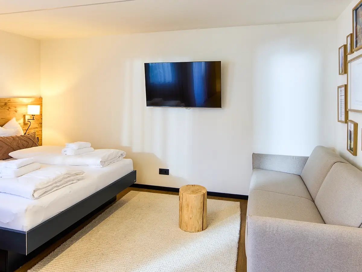 Schlafbereich mit Doppelbett, TV und heller Gestaltung im Apartment HARMONY im Chalet H