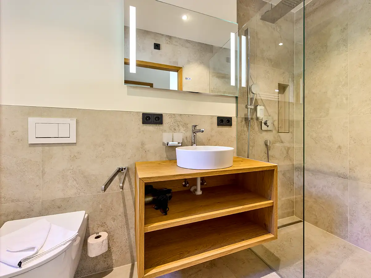 Modernes Badezimmer mit Holzwaschtisch, Spiegel und Glasdusche im Apartment HEIDI im Chalet H