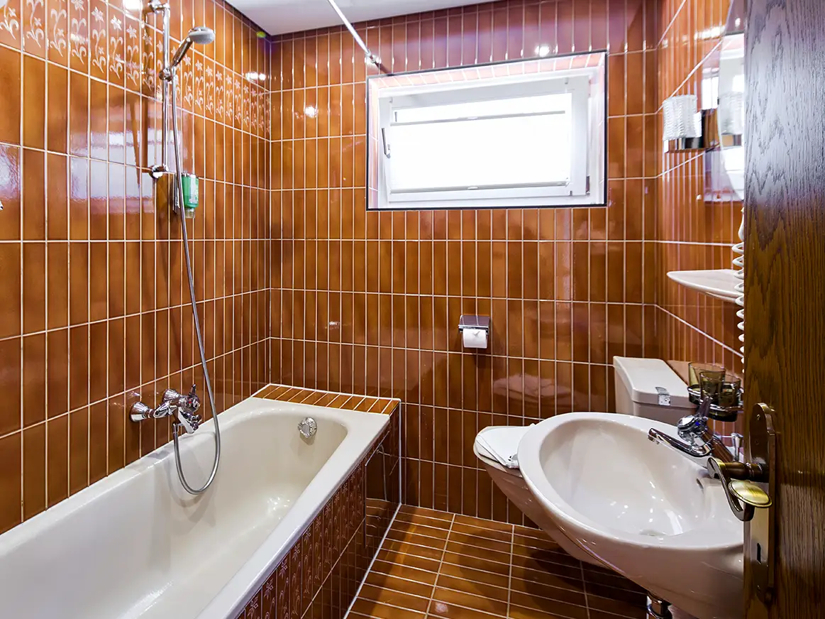 Badezimmer mit Badewanne, WC und warmen Fliesen im Apartment HOME im Chalet H