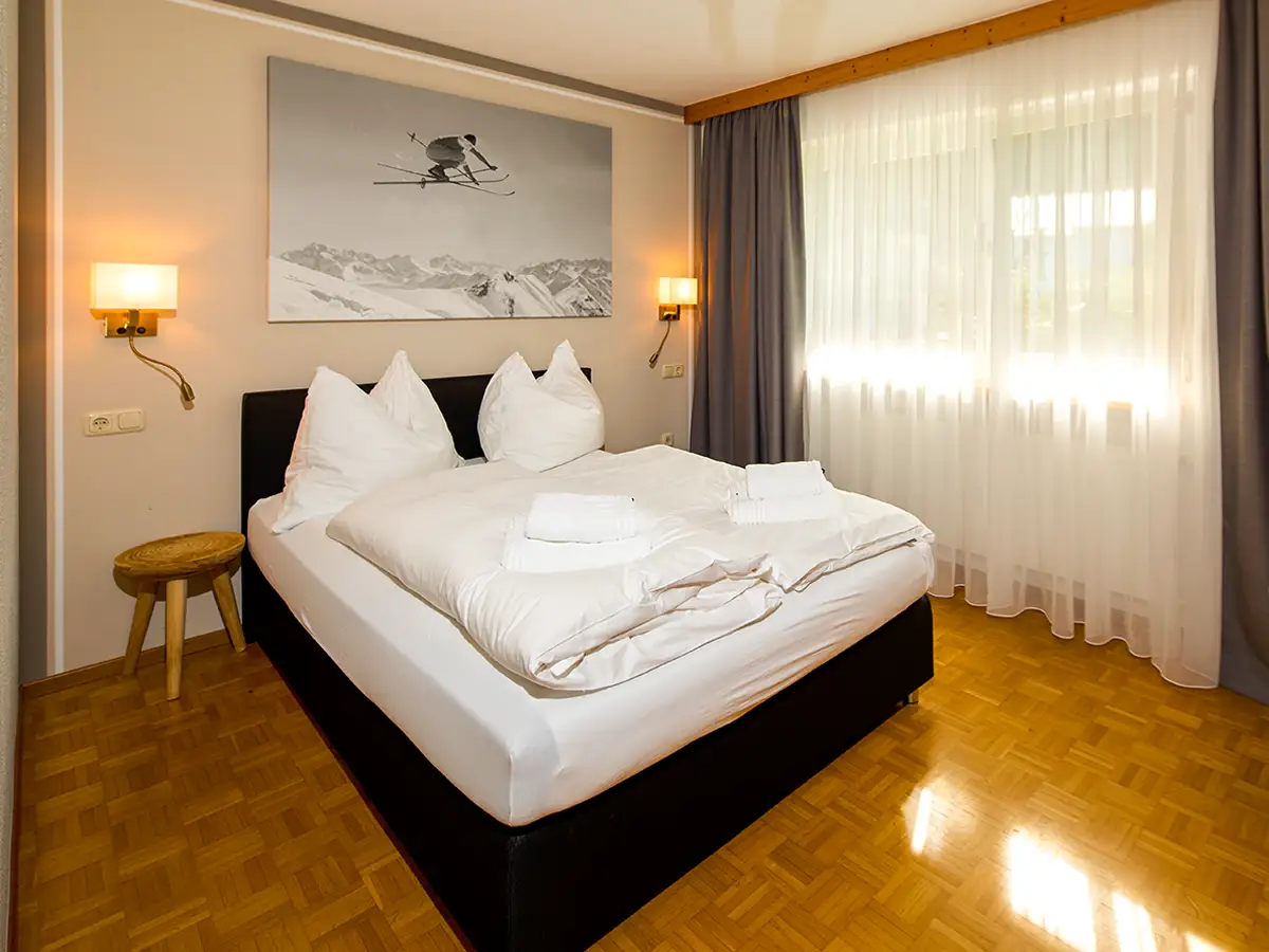 Doppelzimmer mit Holzpaneel, großen Fenstern und heller Bettwäsche im Apartment HOME im Chalet H